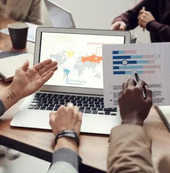 Professionals analyzing charts and a global map on a laptop, representing an offshore software development company's ability to deliver high-quality, cost-effective solutions that ensure financial sustainability and exceptional results.