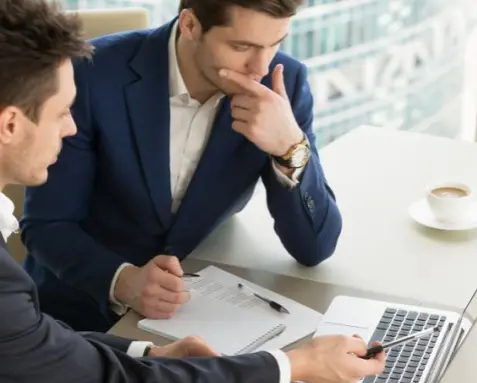 Two professionals reviewing API documentation on a laptop, illustrating a MuleSoft developer providing complete and accessible documentation for use by other developers and stakeholders.