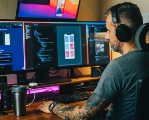 Developer working at a multi-screen setup, coding and designing integration solutions to connect different software applications and services, representing MuleSoft certified developers driving business processes and workflows.