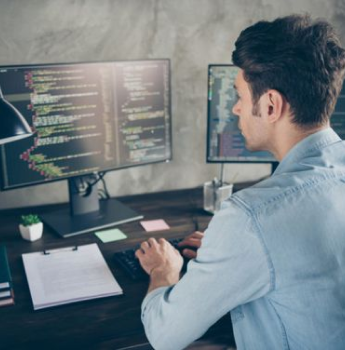 A developer intensely focused on writing code, working at a desk with dual monitors displaying programming scripts, highlighting the efficiency and speed of the development process using Flutter's hot reload feature.