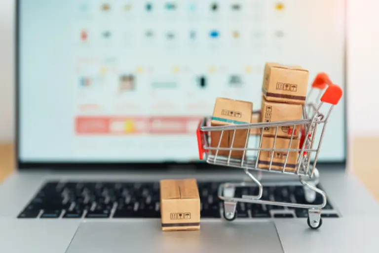 Small shopping cart filled with boxes on a laptop keyboard, representing MuleSoft developers integrating an e-commerce platform with logistics and payment systems for real-time order processing and inventory updates.