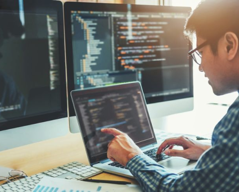 A developer coding on a laptop with multiple screens displaying code, illustrating Samyak Infotech's expertise in full-stack development using AngularJS and back-end technologies like Node.js, Python, and Java.