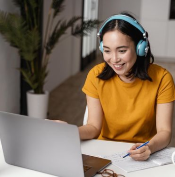 Smiling woman in a yellow shirt with blue headphones working on a laptop, representing educational institutions outsourcing IT functions to manage online learning platforms, maintain secure networks, and provide technical support for quality education delivery.