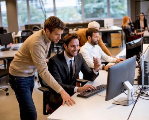 Team members collaborating in a modern office, with one person assisting another at a computer. This image represents Samyak Infotech’s staff augmentation services, providing flexible, skilled IT professionals to supplement existing teams, ensuring scalability, agility, and enhanced productivity for clients.