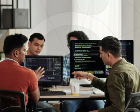 A dedicated team of IT professionals collaborating around computers with code on their screens. This image illustrates Samyak Infotech's dedicated team model, where IT experts work exclusively on clients' projects, providing continuous innovation, technical expertise, and seamless integration with the client's internal team for long-term success.