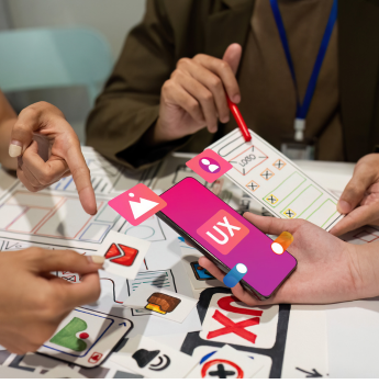 Group of developers working on a mobile app design, discussing and pointing at a smartphone with UX/UI elements to ensure a consistent user experience across all platforms.