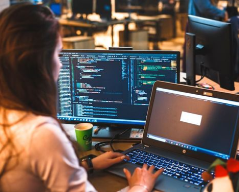 A developer working on a laptop and monitor with code displayed, representing Samyak Infotech's web app migration services to AngularJS, ensuring efficient and user-friendly applications with minimal operational disruption.