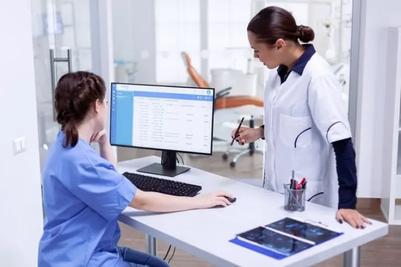 Two healthcare professionals reviewing data on a computer screen in a medical office, highlighting the use of Power Automate services to automate compliance reporting, reduce manual work, and minimize errors in the healthcare sector.