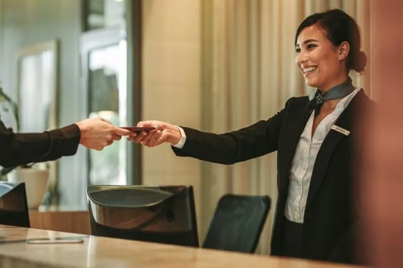 Smiling hotel receptionist handing a guest a document, representing the implementation of an offshore software solution for a large hotel chain, which centralized reservation management and improved customer service, leading to increased booking accuracy and customer satisfaction.