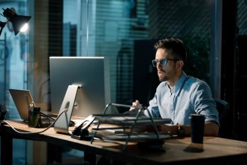 A focused professional working on a computer late at night, representing the development of customized Natural Language Processing software solutions for machine learning applications.