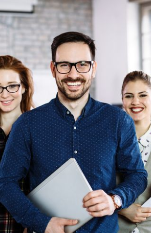 A smiling team of professionals, including a man holding a laptop, representing the collaborative and communicative culture fostered by DevOps consulting services to improve teamwork and problem-solving.