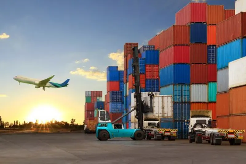 Cargo containers stacked at a shipping yard with a forklift in operation and an airplane taking off in the background, illustrating optimized logistics operations through cloud DevOps consulting services.