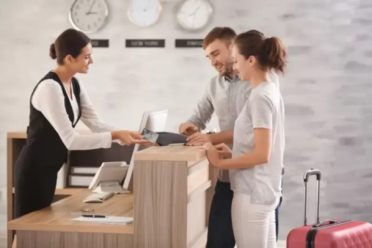 A hotel receptionist assisting a couple at the front desk, highlighting the use of custom AI solutions to improve guest experiences, increase direct bookings, and optimize revenue management in the hospitality industry.