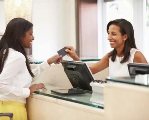 A hotel receptionist assisting a guest at the front desk, illustrating the use of Power Automate services to automate the check-in process for higher efficiency and accuracy in the hospitality industry.