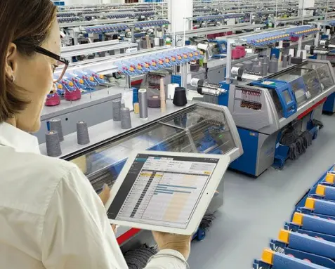 Manufacturing professional using a tablet to monitor production lines in a factory, symbolizing offshore software development services that enhance manufacturing operations through ERP systems, IoT-enabled tools, and predictive maintenance.